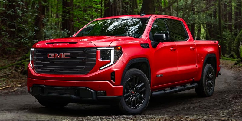 Red GMC Sierra 1500 Driving on a road through a forest