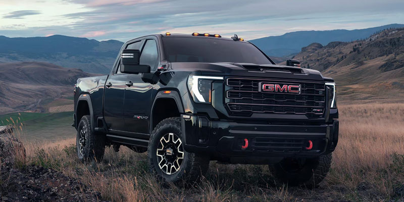A rugged black GMC Sierra 2500HD driving through an open field with mountainous terrain in the background.